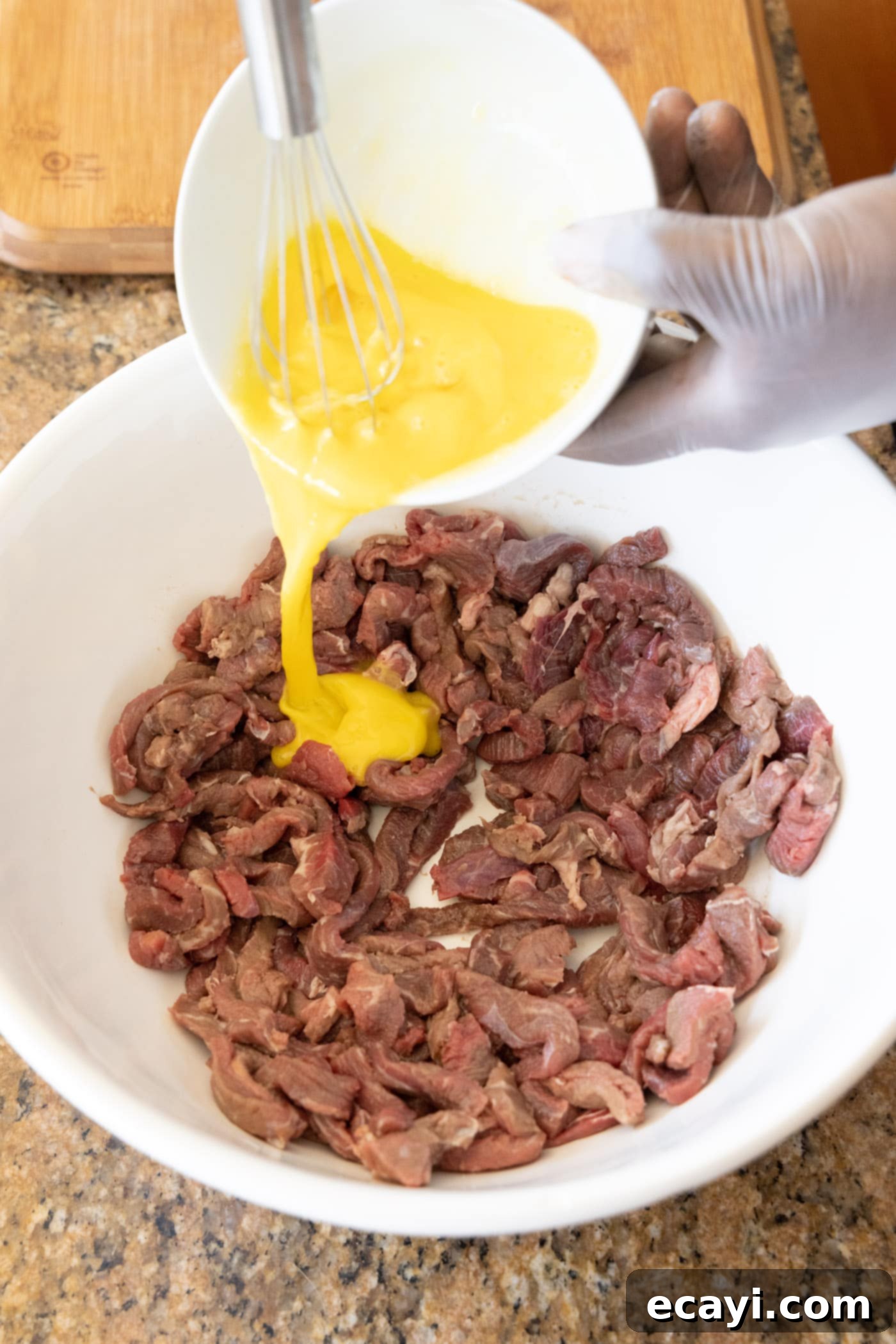 Crispy Beijing Beef 6 Sliced flank steak soaking in whisked egg, preparing for the cornstarch coating.