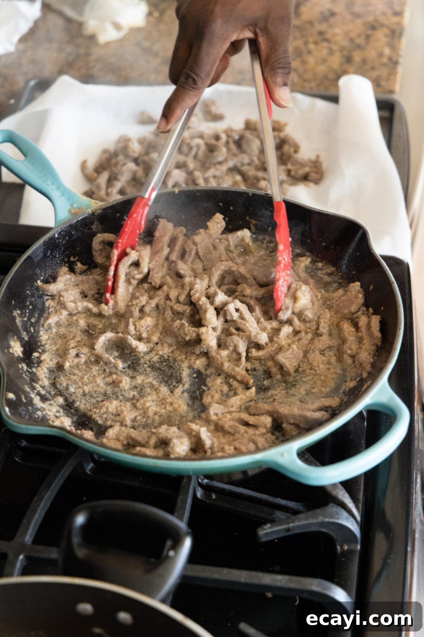 Crispy Beijing Beef 8 Tongs lifting crispy, cooked beef strips from a hot skillet, ready to be set aside.