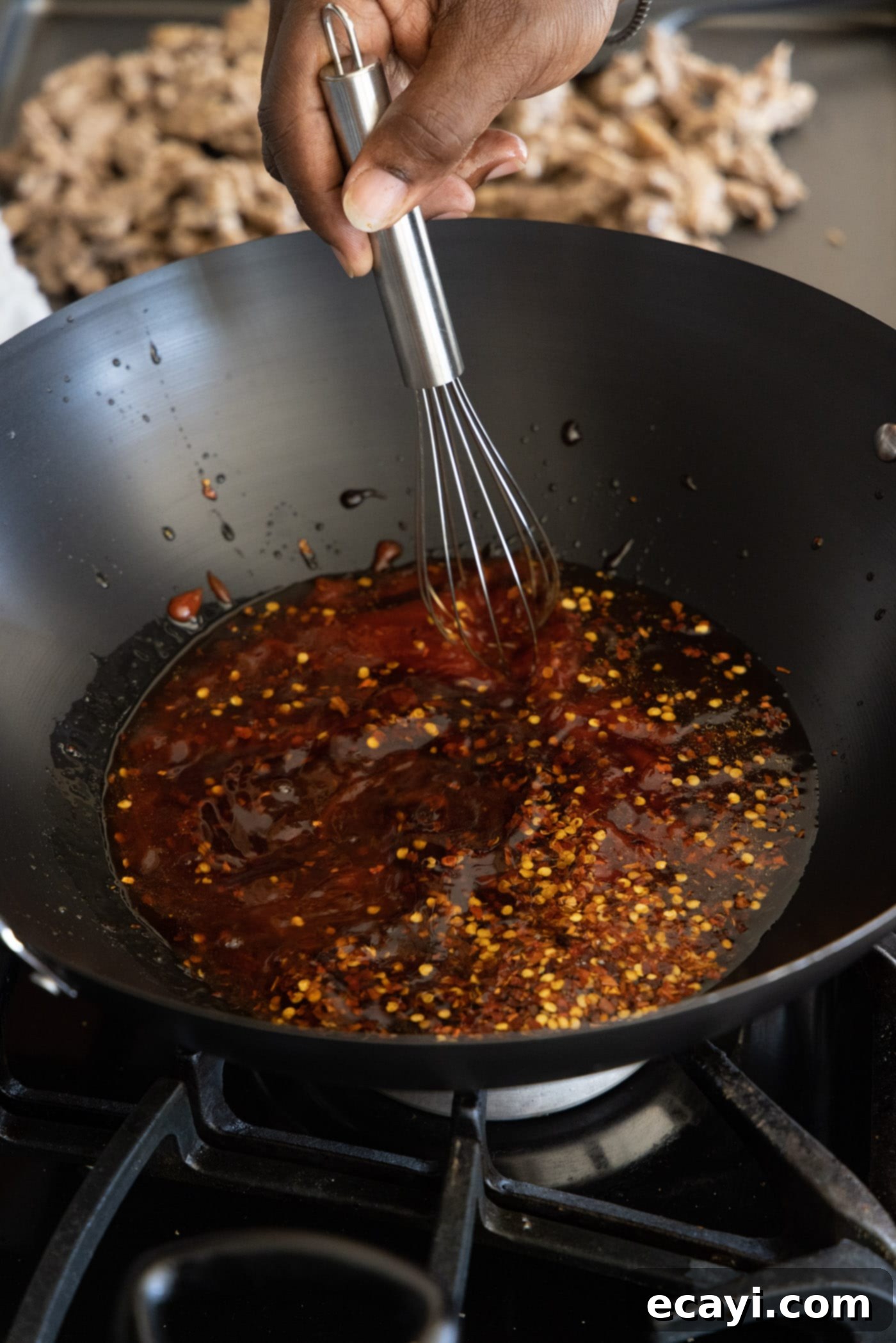 Crispy Beijing Beef 10 A whisk stirring the homemade Beijing Beef sauce ingredients in a wok, bringing it to a simmer.