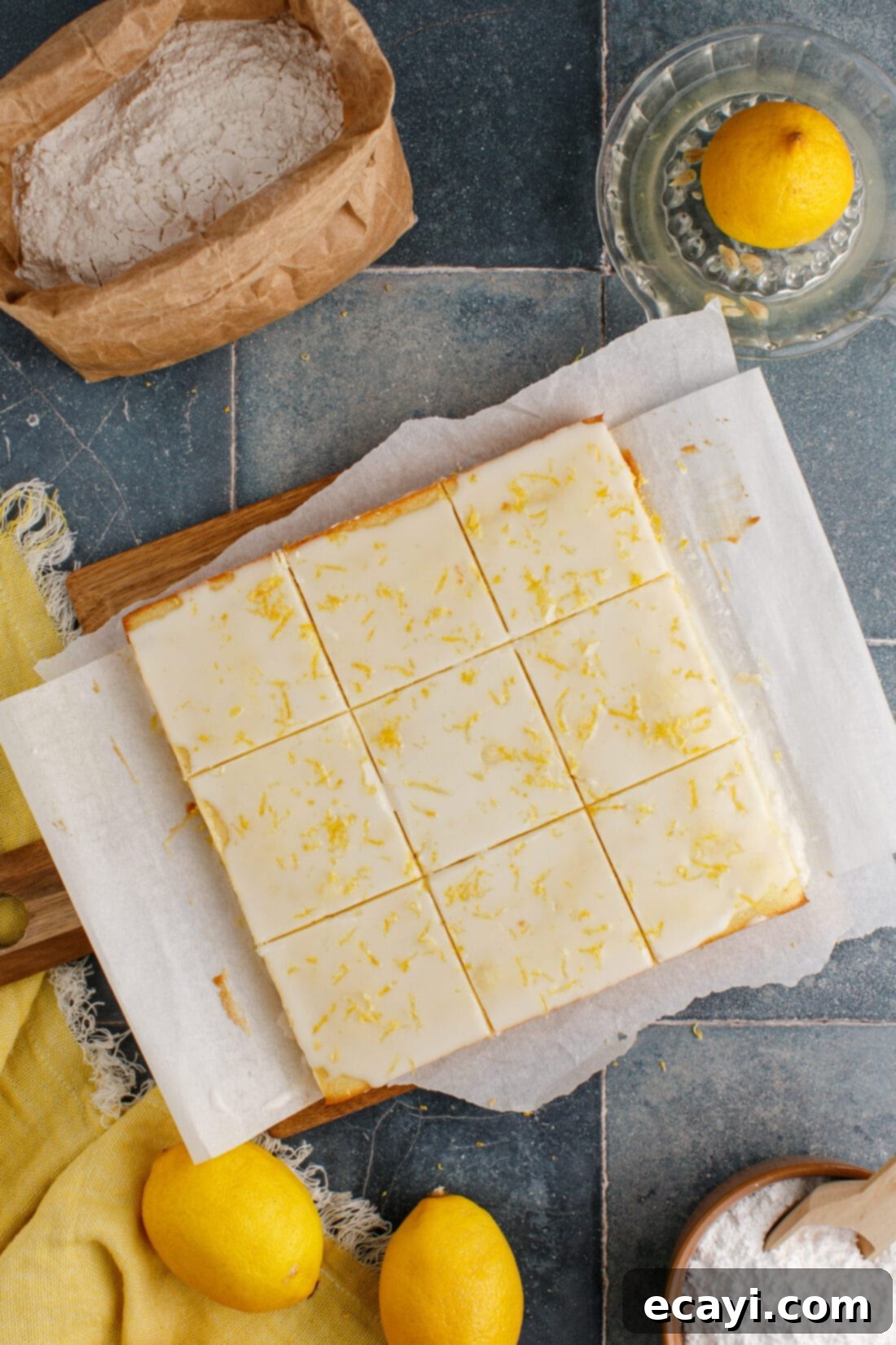 Sunshine Lemon Brownies 2 Lemon Brownies cut into squares on a wooden cutting board, glistening with lemon glaze