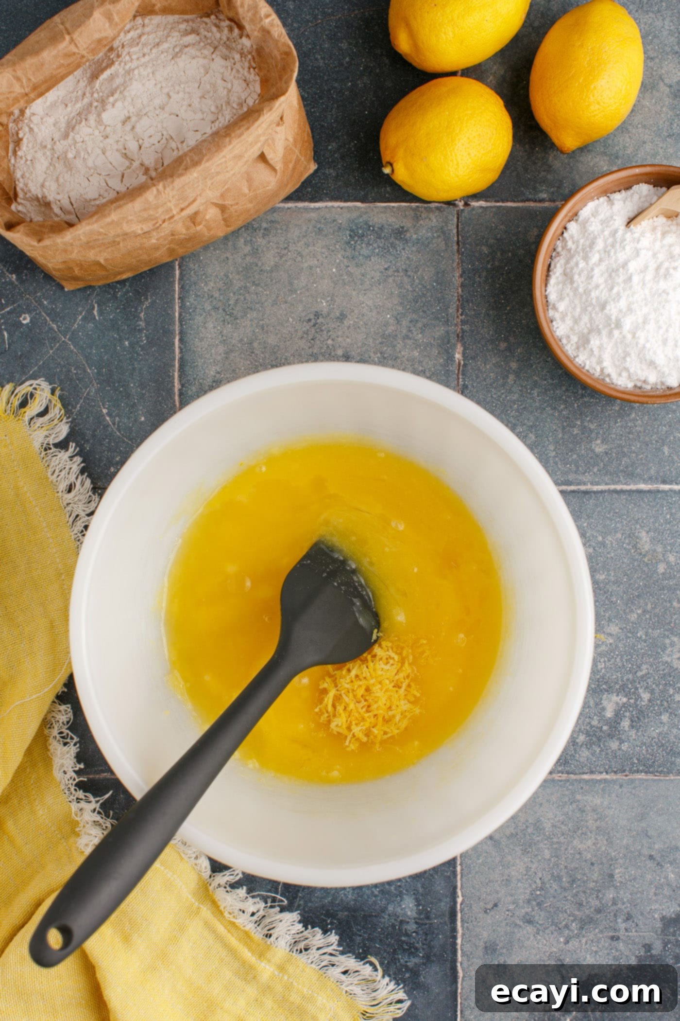 Sunshine Lemon Brownies 6 lemon juice and zest added to butter mixture in bowl, being mixed with a spatula