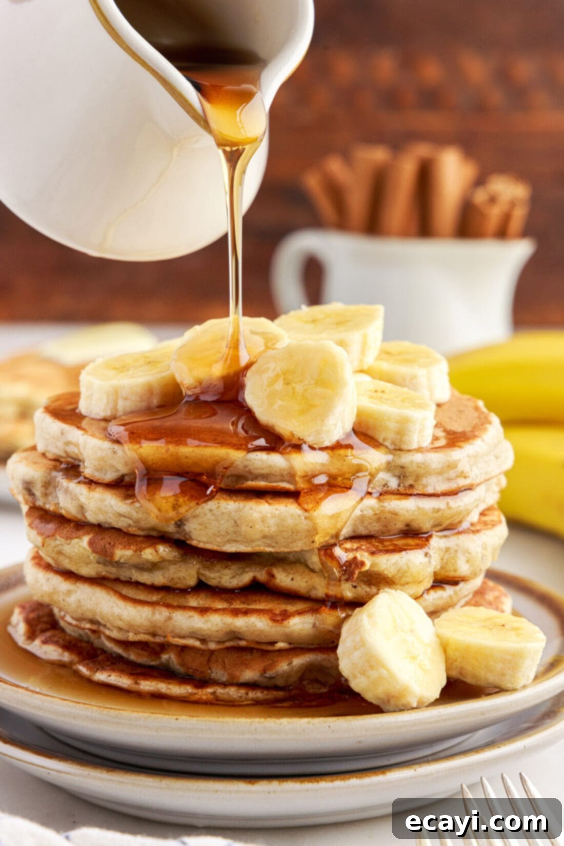 Fluffy Banana Bliss 2 Stack of Golden Brown Banana Pancakes with maple syrup being drizzled on top, a fork resting on the side