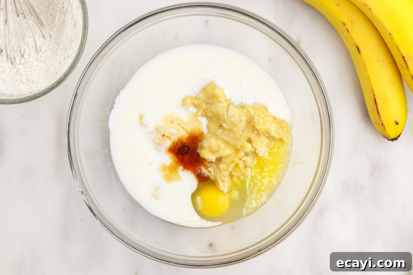 Fluffy Banana Bliss 7 Wet ingredients for banana pancake batter including egg, melted butter, vanilla, buttermilk, and mashed banana in a large bowl