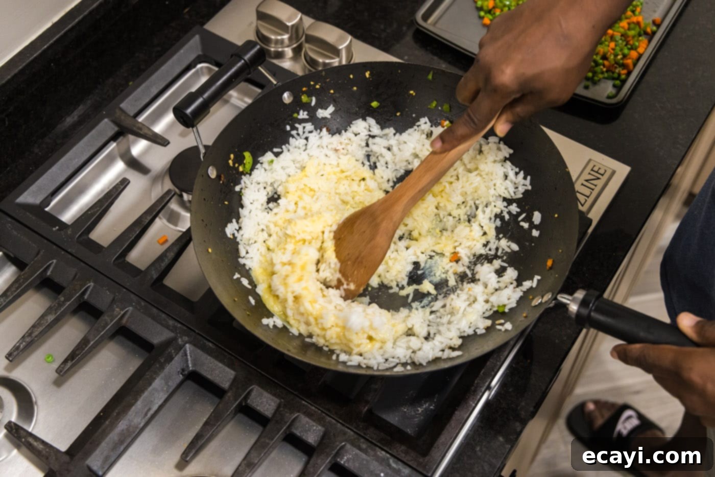 Wok-Fired Pork Fried Rice 13 A wooden spoon mixing scrambled eggs into white rice in a large skillet