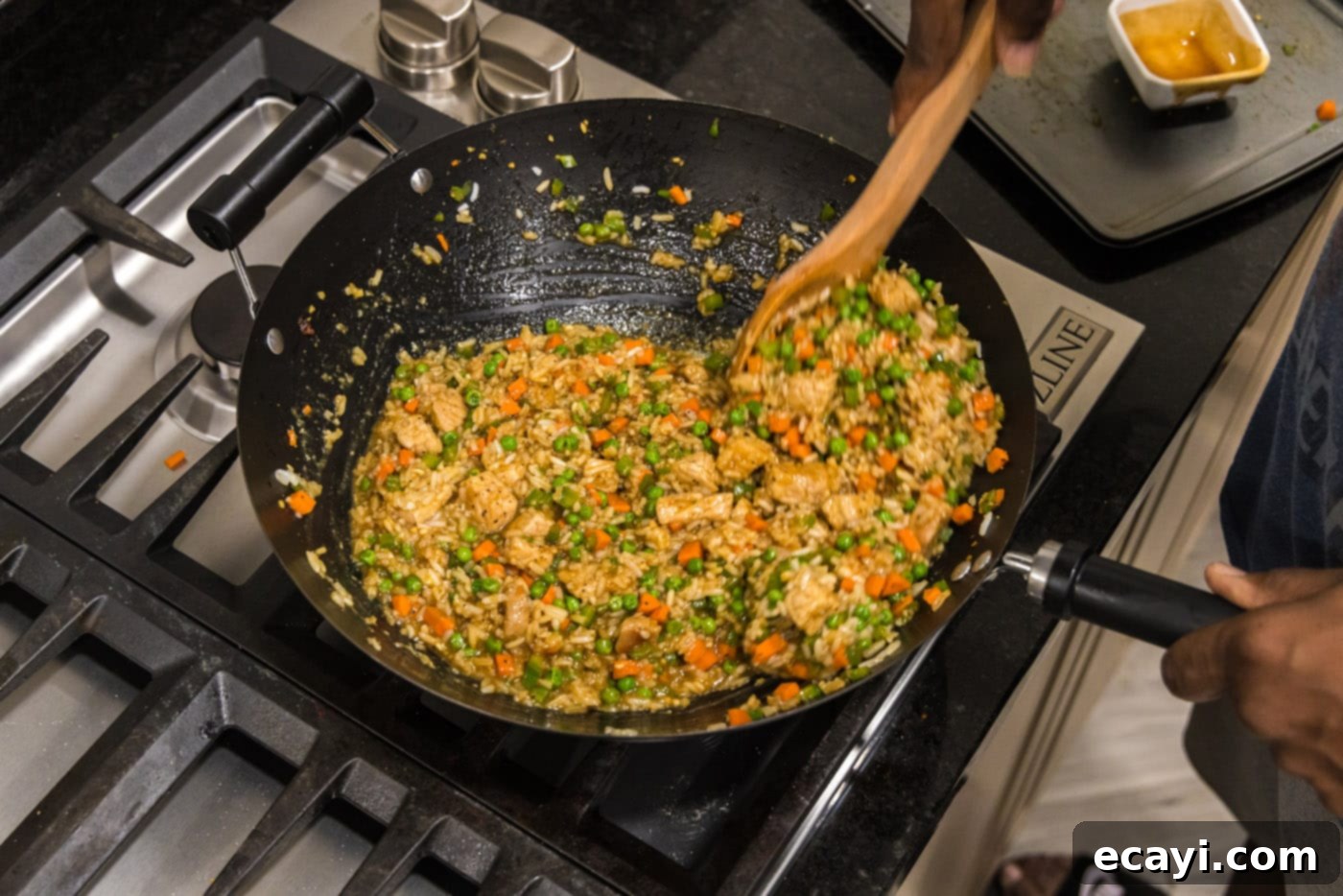 Wok-Fired Pork Fried Rice 17 A wooden spoon actively mixing the ingredients of pork fried rice in a wok, showing the colorful mix coming together