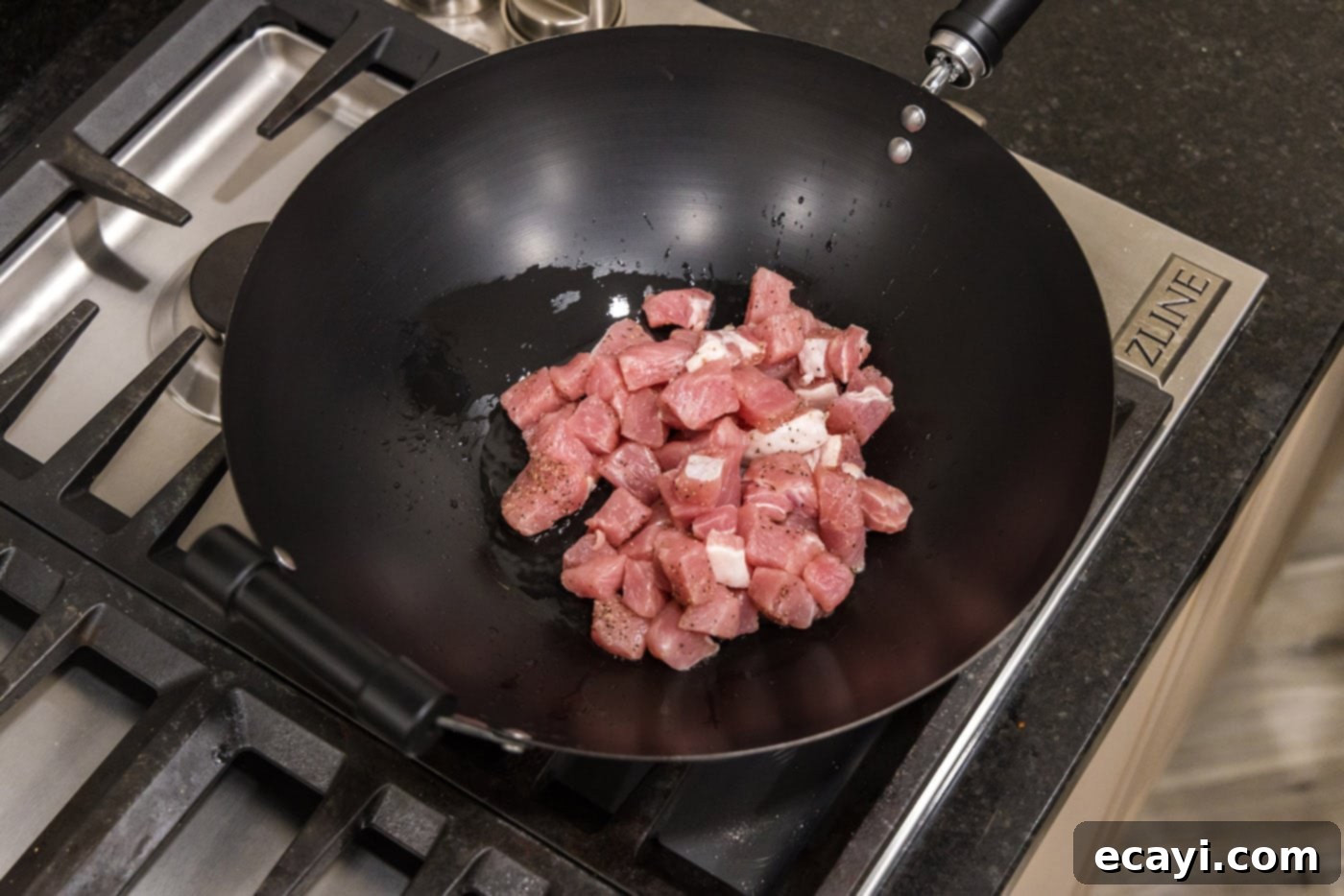 Wok-Fired Pork Fried Rice 7 Raw diced pork chops being added to hot olive oil in a wok for stir-frying