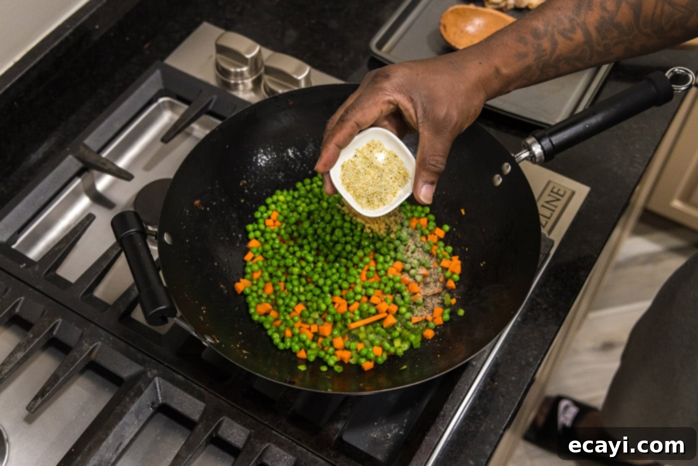 Wok-Fired Pork Fried Rice 9 Hand adding a sprinkle of seasonings to a mix of green bell pepper, carrots, and peas in a hot wok