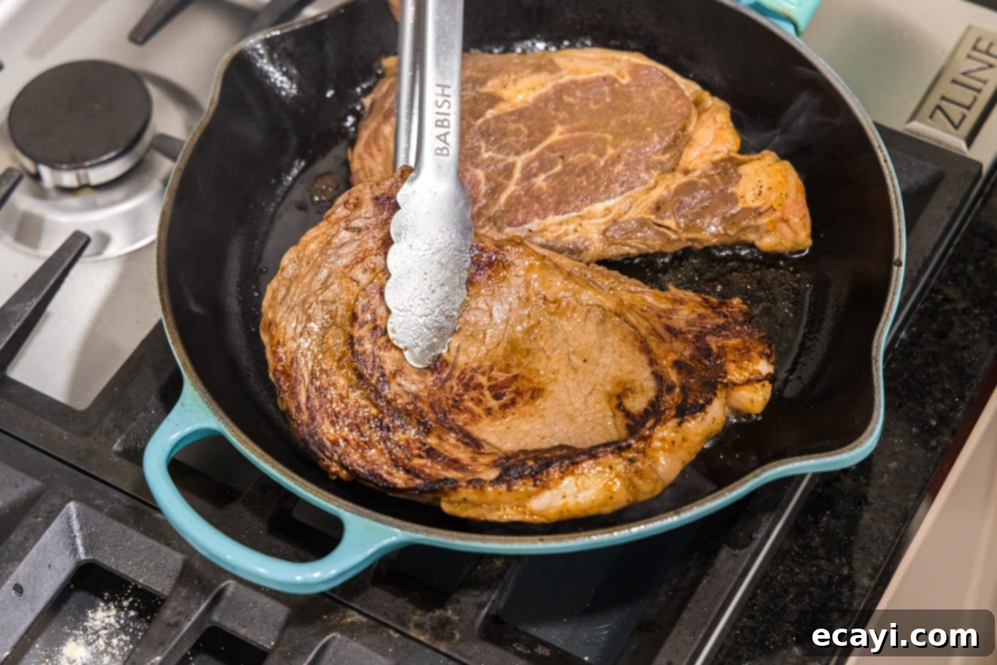 The Ultimate Cast Iron Ribeye 7 Tongs flipping ribeye steak over in a cast iron skillet to sear the other side