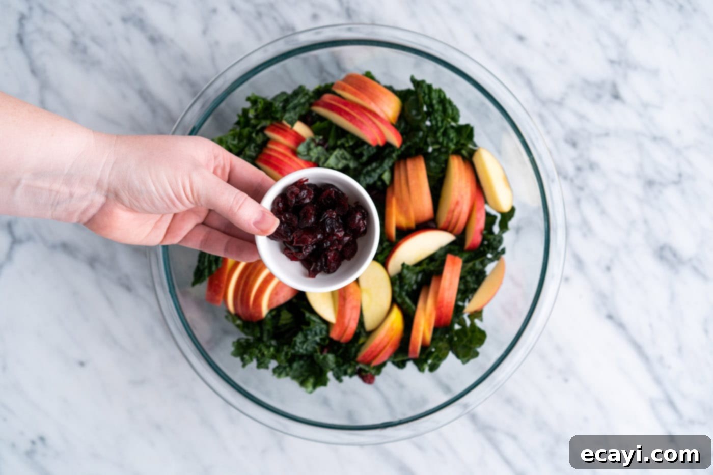 Signature Kale Salad 8 adding craisins to apples and kale in a bowl