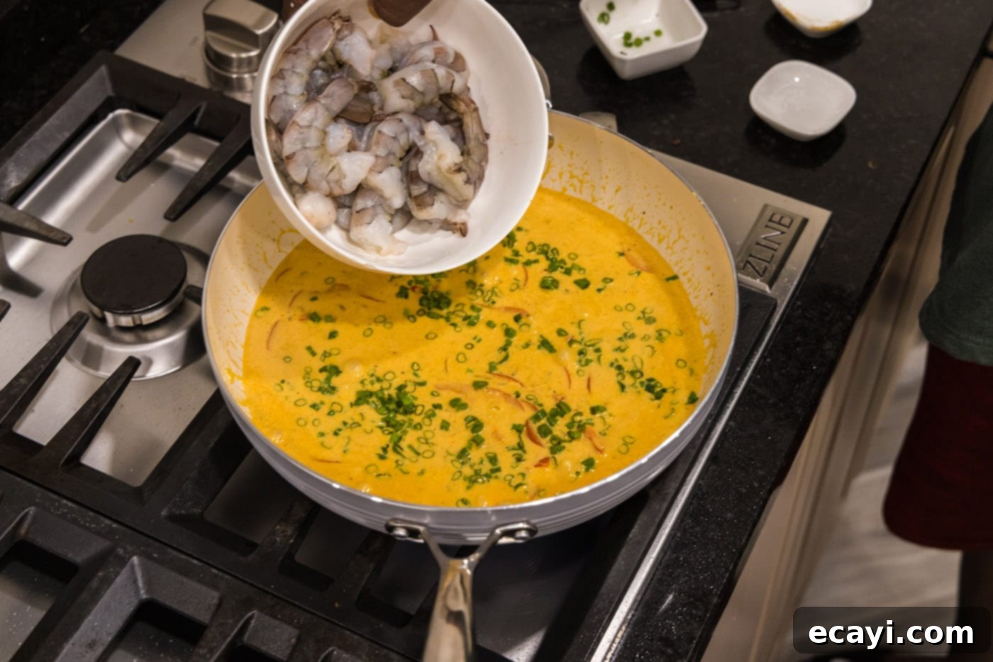 Mouthwatering Shrimp Curry 10 Raw, deveined shrimp and chopped green onions being added to the rich curry sauce in the skillet, ready to cook and absorb the flavors.
