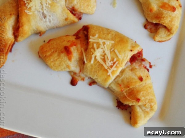 Cheesy Pizza Crescents 4 A close up overhead photo of a single, perfectly golden-baked pizza crescent roll up on a white platter, revealing its flaky layers and tempting cheesy filling.