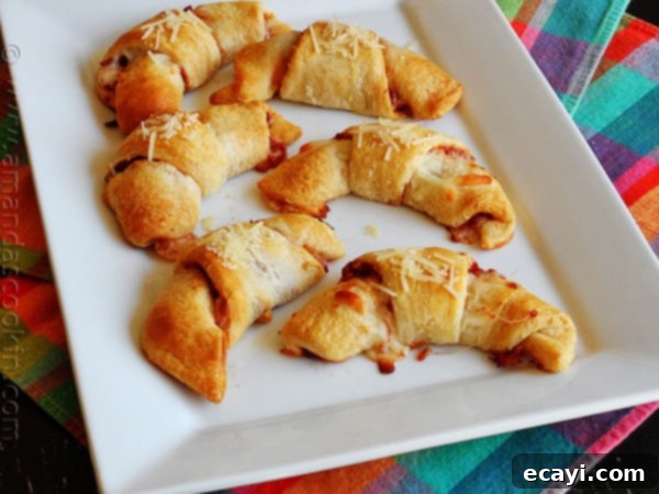 Cheesy Pizza Crescents 7 An overhead photo of a white platter filled with perfectly golden, baked pizza crescent roll ups, garnished and ready for serving to a crowd.