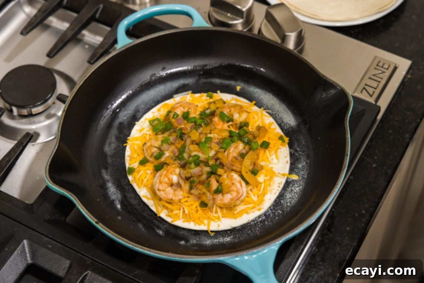 Zesty Shrimp Quesadilla 10 A close-up view of shrimp, cheese, and sautéed vegetables arranged on a tortilla in a skillet.