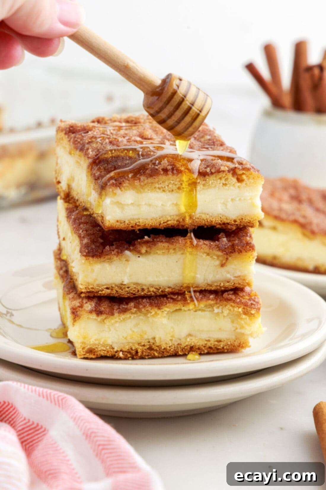 Cinnamon Swirl Sopapilla Cheesecake 2 Honey drizzled generously over a stack of perfectly cut Sopapilla Cheesecake squares, highlighting their golden crust and inviting sweetness.