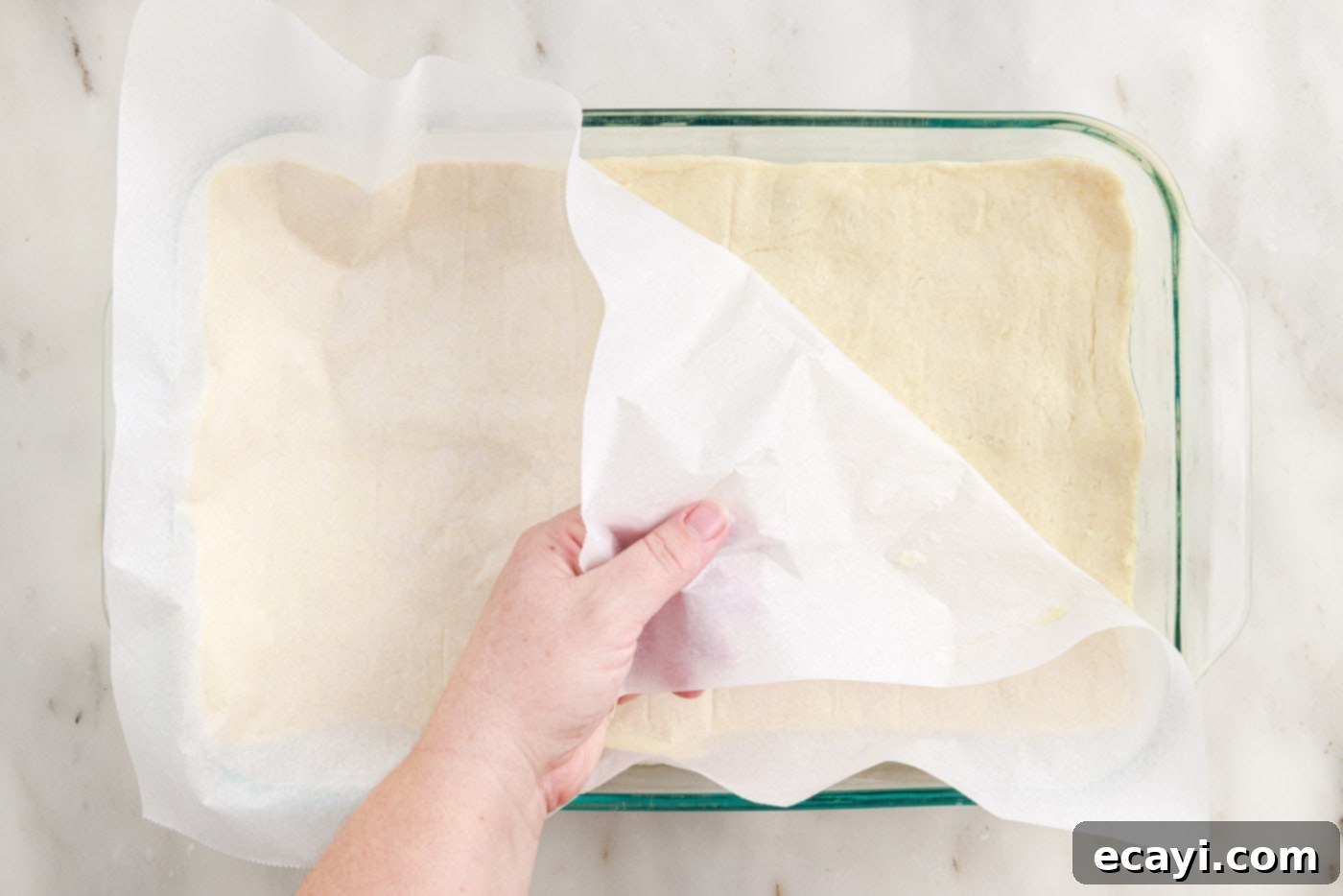Cinnamon Swirl Sopapilla Cheesecake 12 The process of gently peeling parchment paper away from the crescent dough, which now forms the top layer over the cheesecake filling.