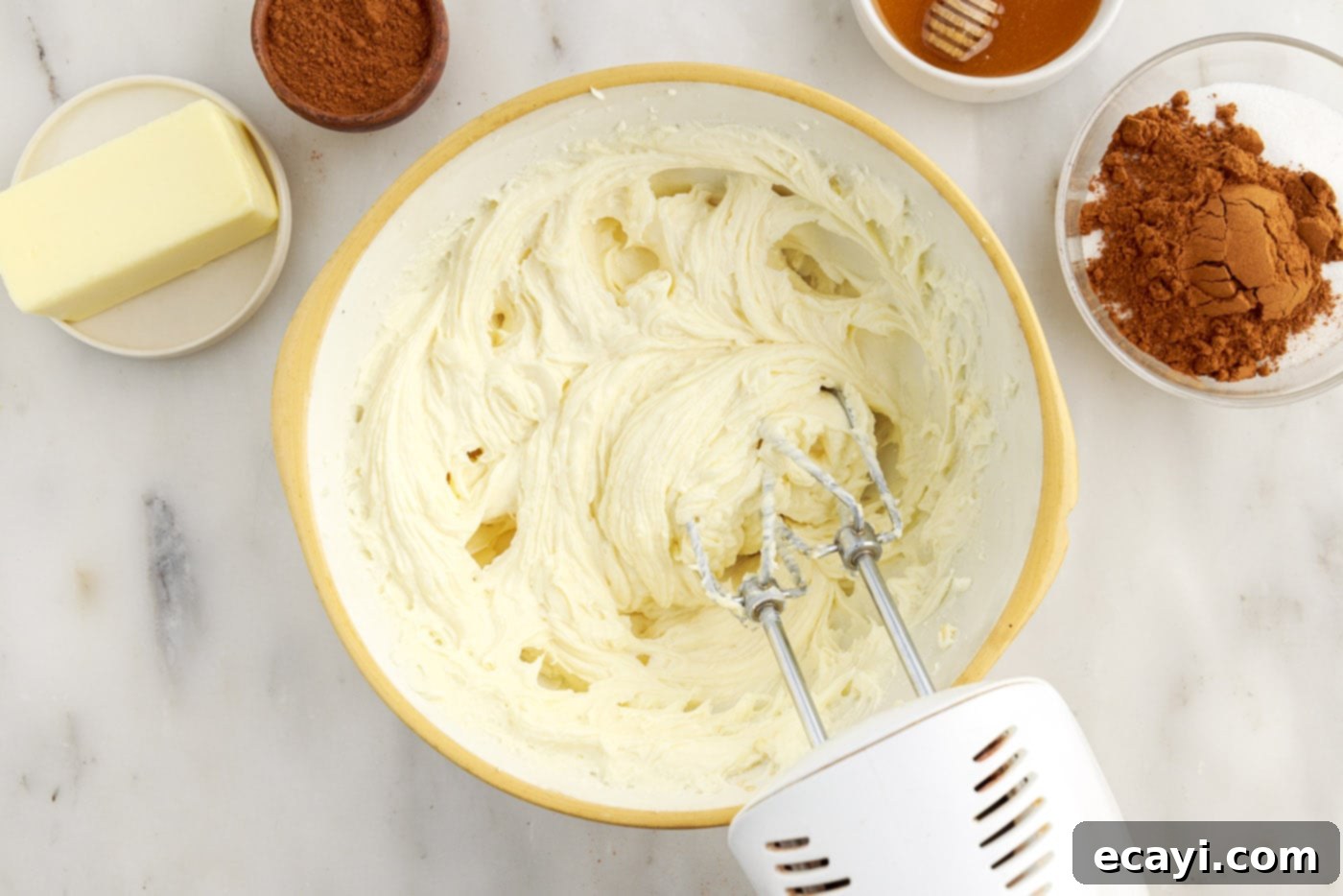 Cinnamon Swirl Sopapilla Cheesecake 7 A hand mixer vigorously blending cream cheese with vanilla and sugar in a bowl, creating a smooth and airy cheesecake filling.