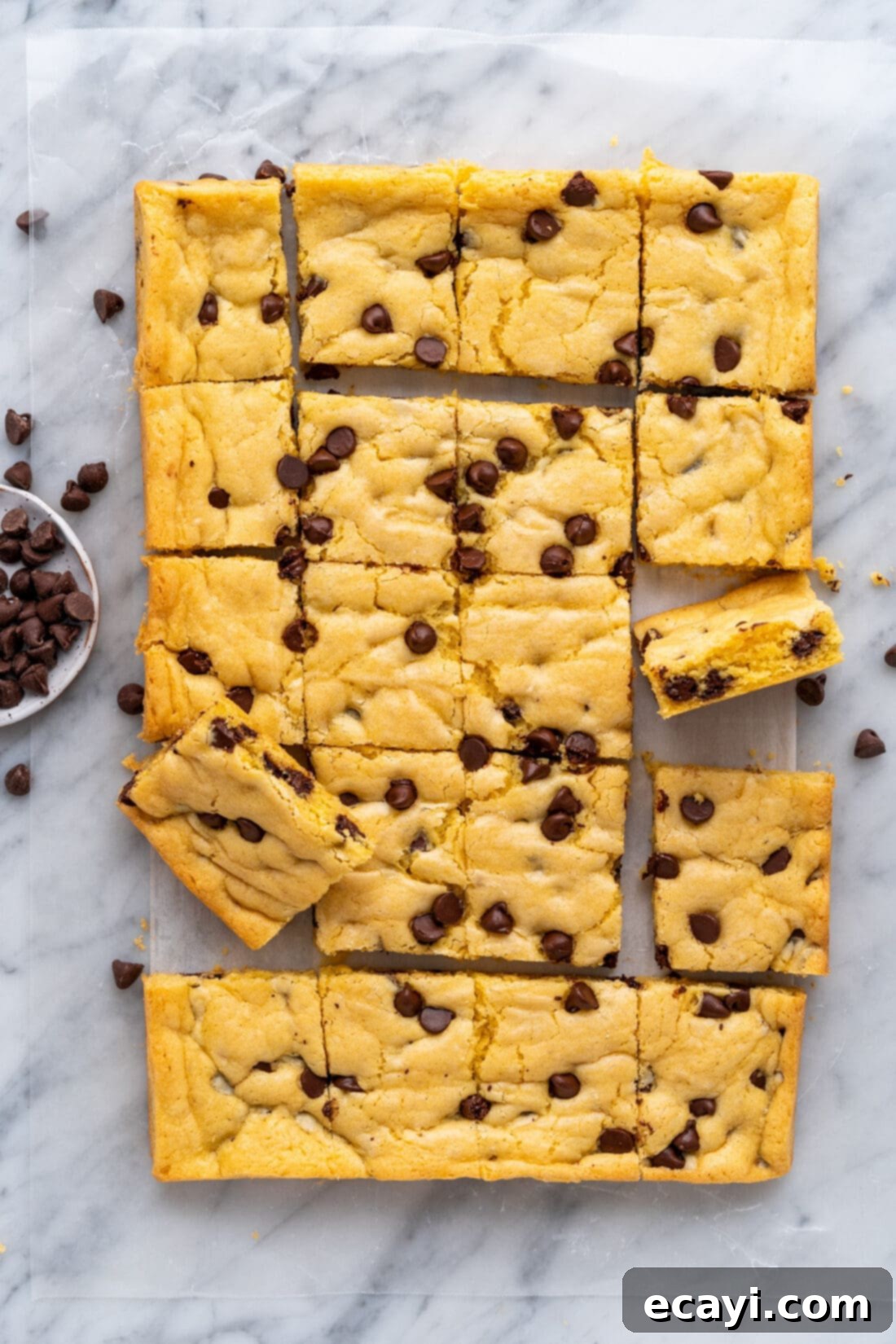 Easy Cake Mix Cookie Bars 2 A sheet of freshly baked Cake Mix Cookie Bars cut into squares, resting on parchment paper, highlighting their golden edges and abundant chocolate chips.
