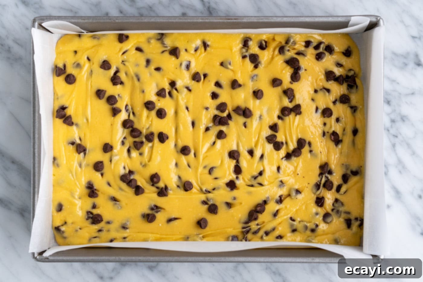 Easy Cake Mix Cookie Bars 11 Additional chocolate chips sprinkled generously over the top of the raw cake mix cookie bar batter in the baking pan, ready for the oven.