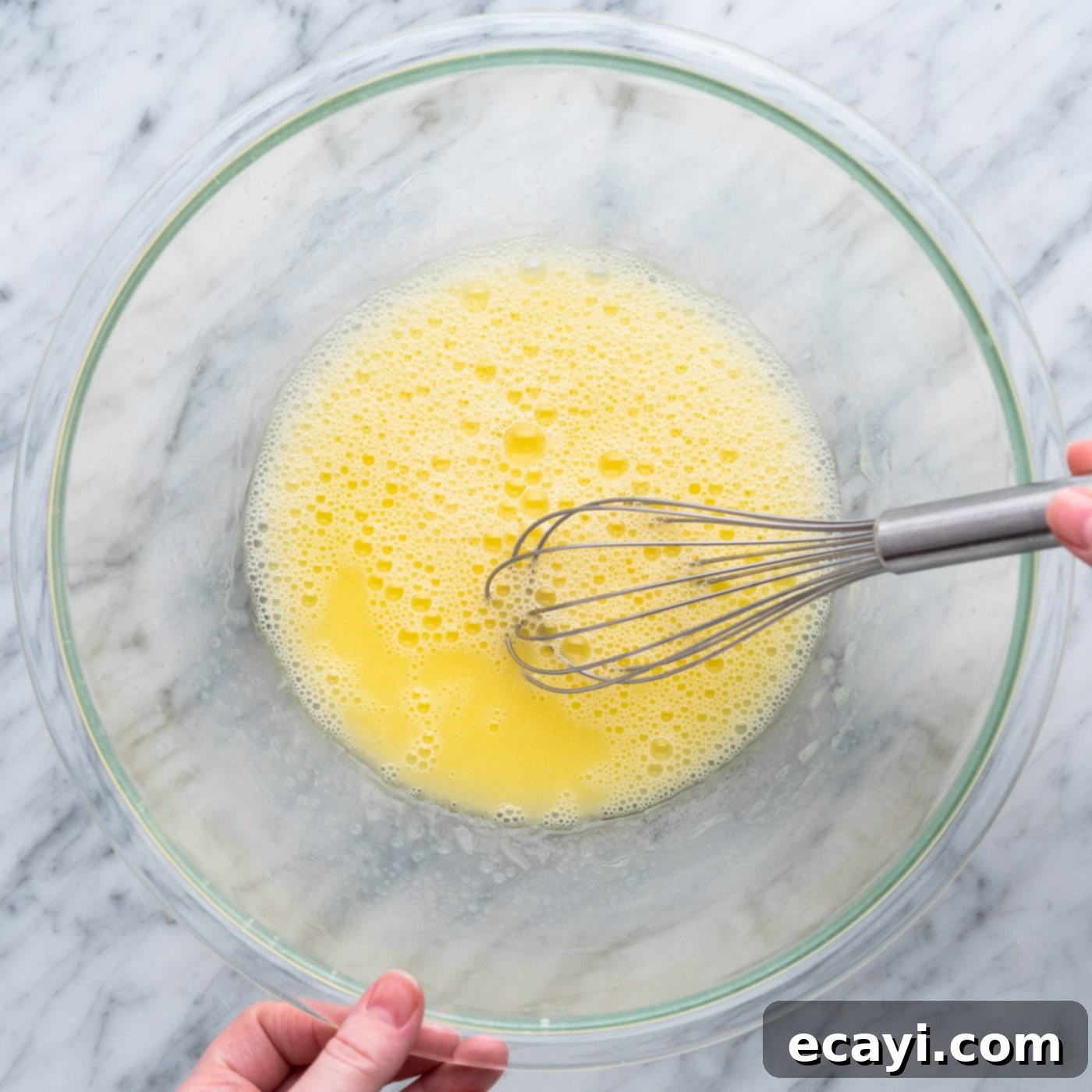 Easy Cake Mix Cookie Bars 5 A hand whisking together vegetable oil, water, and an egg in a clear mixing bowl, creating a smooth yellow mixture for the cookie bars.