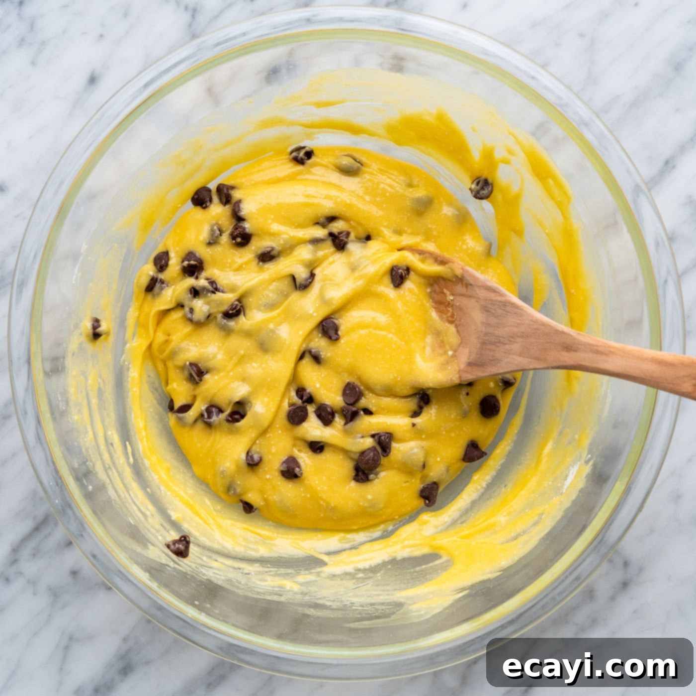 Easy Cake Mix Cookie Bars 8 A wooden spoon stirring chocolate chips into the thick cake mix cookie bar batter in a mixing bowl.