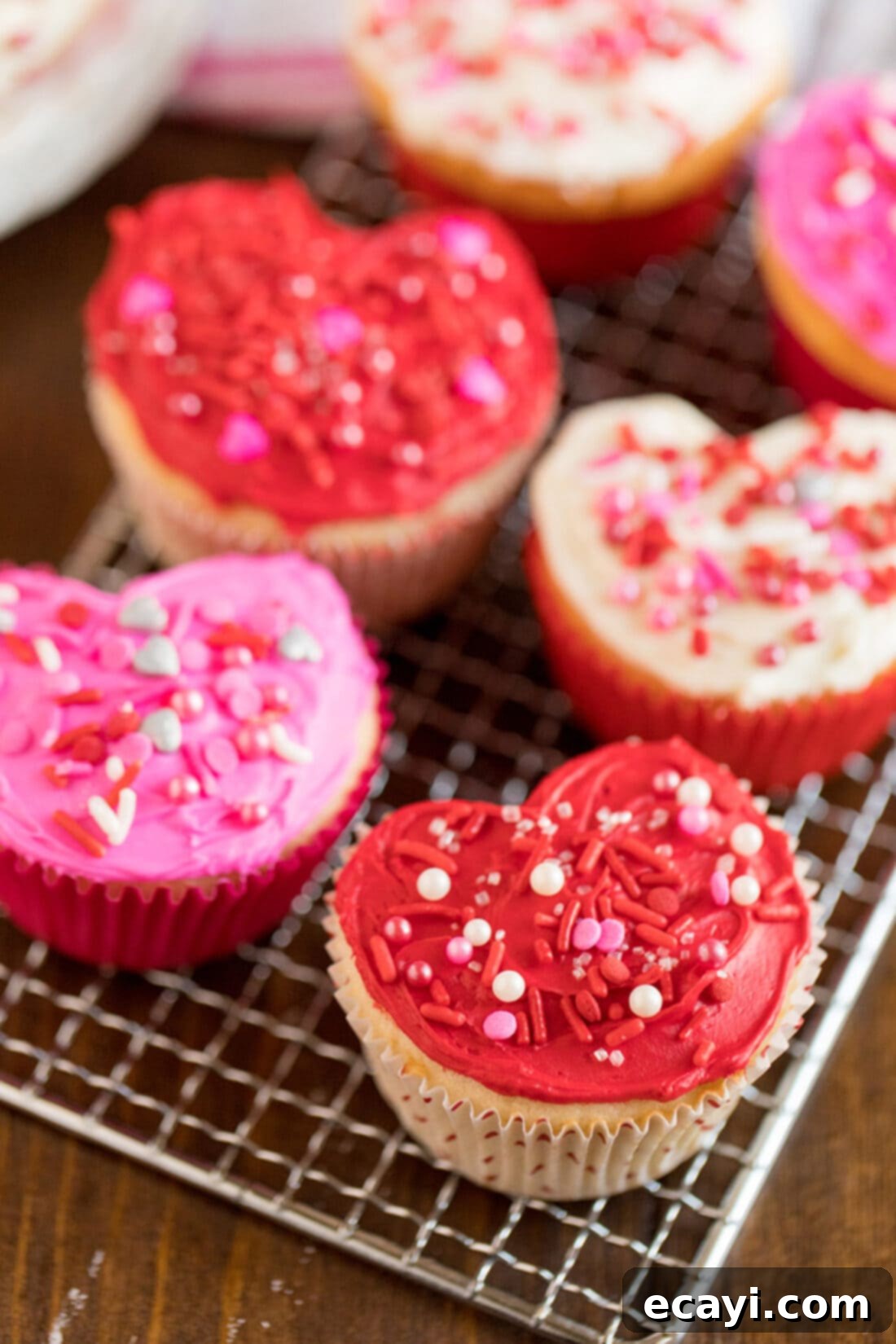 These heart cupcakes are shaped like hearts and covered in white, pink and red frosting. Make these super easy Valentine cupcakes from scratch or a box! #valentinesday #valentinesdaytreats #desserts #love #valentines #cupcakes #cupcakerecipes #cake #anniversary Heart shaped cupcakes on a cooling rack, freshly baked and ready for frosting.