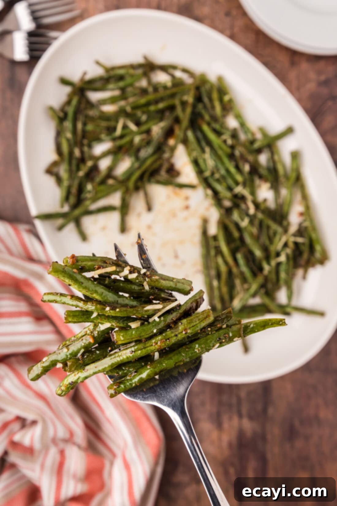 Crispy Roasted Green Beans 2 Serving fork full of Roasted Green Beans held above a platter of perfectly roasted green beans seasoned with garlic and soy sauce