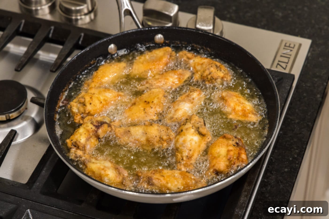 Crispy Fried Chicken Wings 11 fried chicken wings glistening in a skillet of oil, ready to be removed.