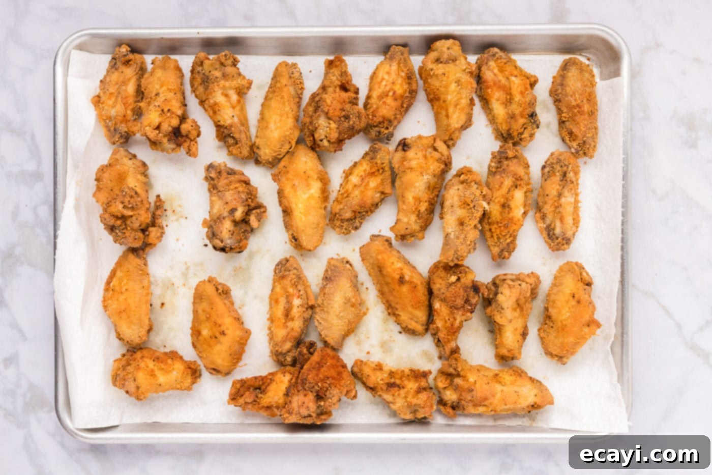 Crispy Fried Chicken Wings 12 fried chicken wings resting on a baking sheet lined with paper towels, draining excess oil.