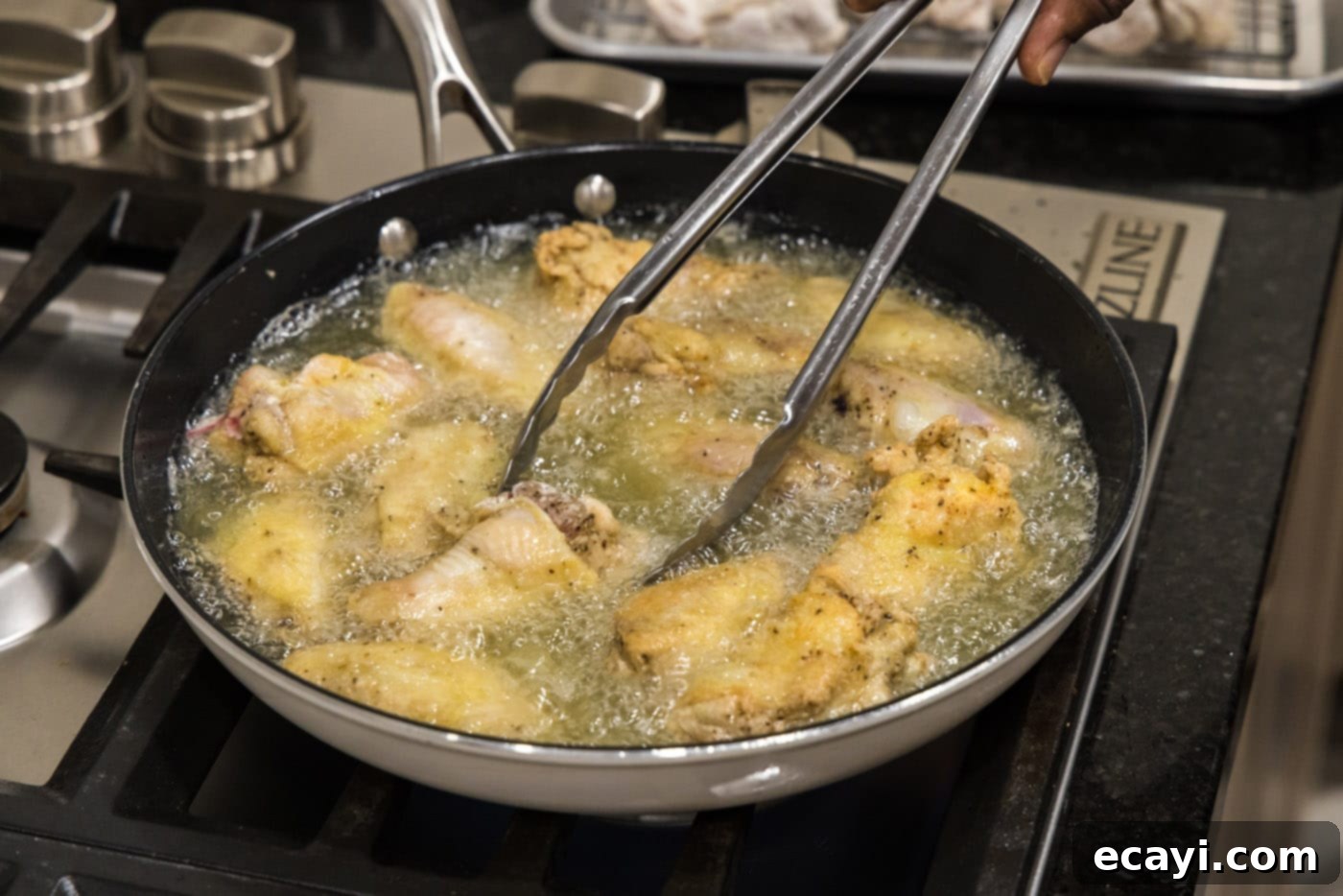 Crispy Fried Chicken Wings 10 tongs flipping chicken wings in a skillet, showing the browning process.