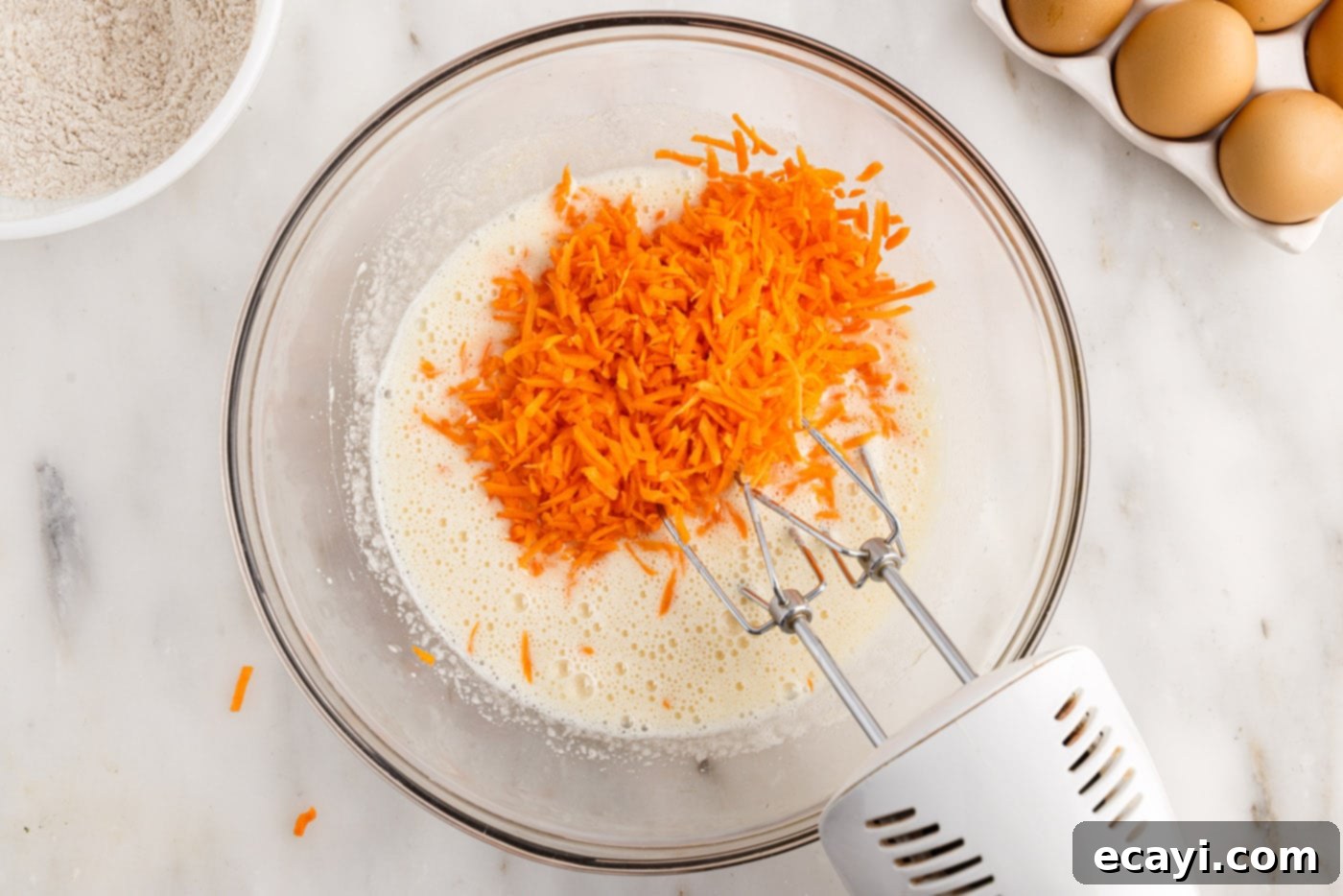 Swirled Carrot Delight 6 Finely grated carrots, vanilla, and vegetable oil being added to the egg mixture in a bowl.