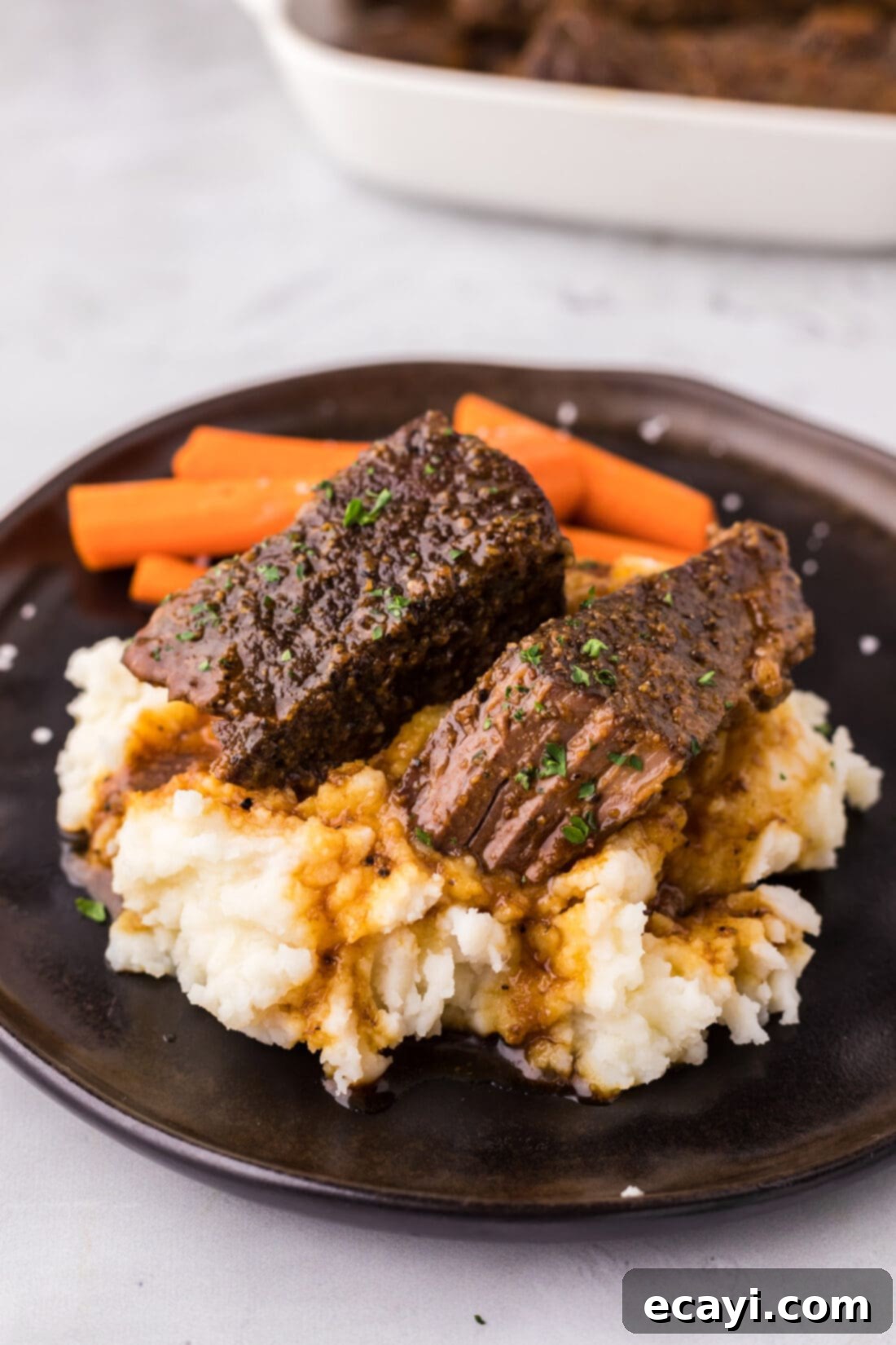 Tender Boneless Beef Short Ribs 2 Boneless Beef Short Ribs served over creamy mashed potatoes on a white plate, garnished for a perfect meal.