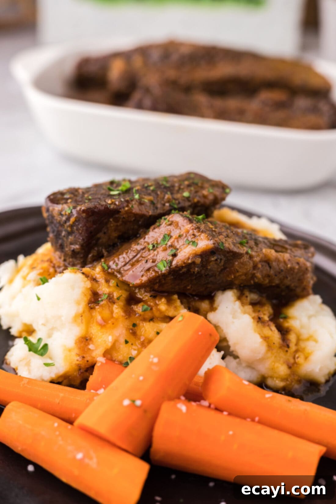 Tender Boneless Beef Short Ribs 12 Plated boneless beef short ribs on a bed of creamy mashed potatoes, accompanied by vibrant roasted carrots, showcasing a complete and appetizing meal.