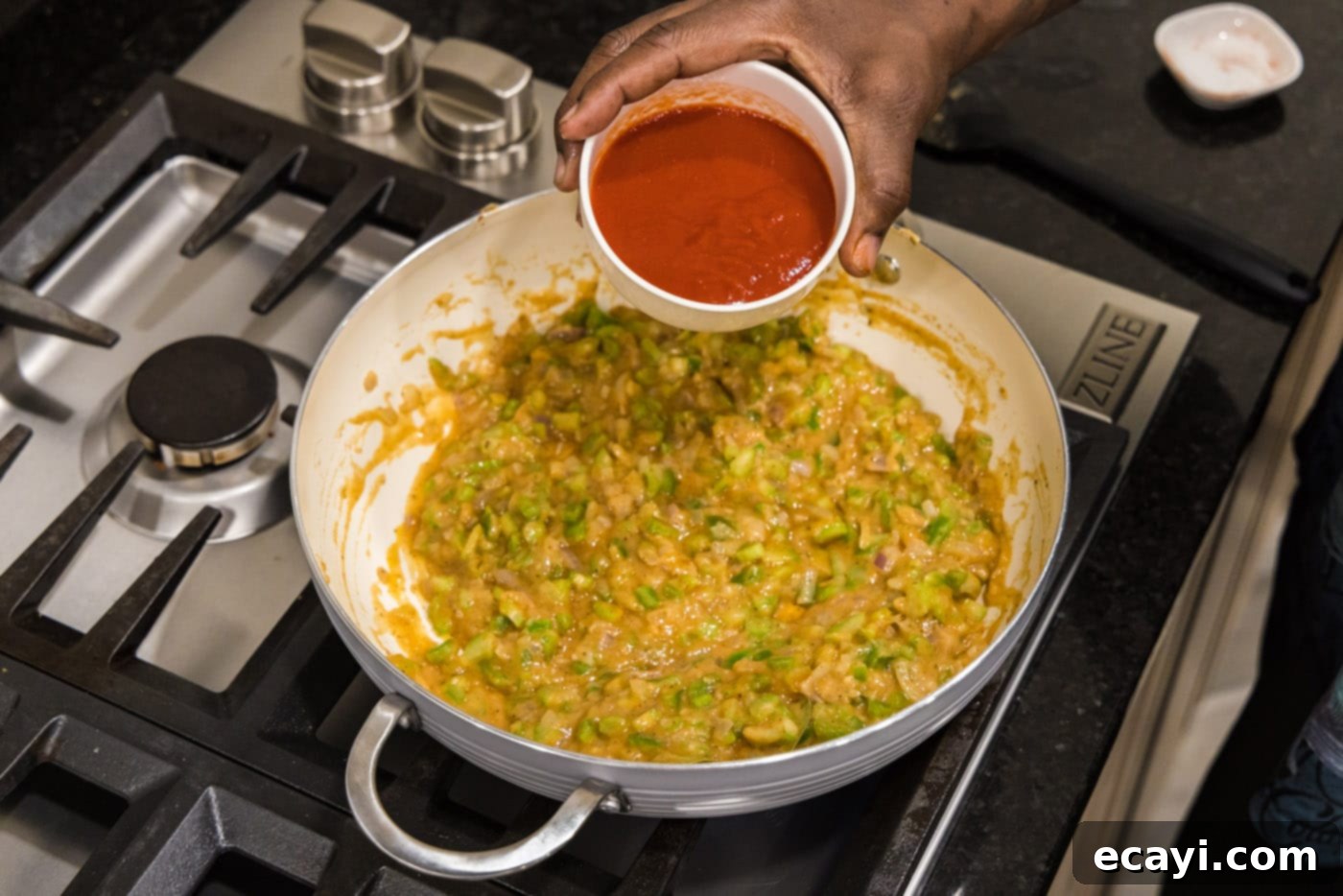 Crawfish Etouffee: A Taste of Louisiana 11 pouring tomato sauce into skillet with vegetable roux