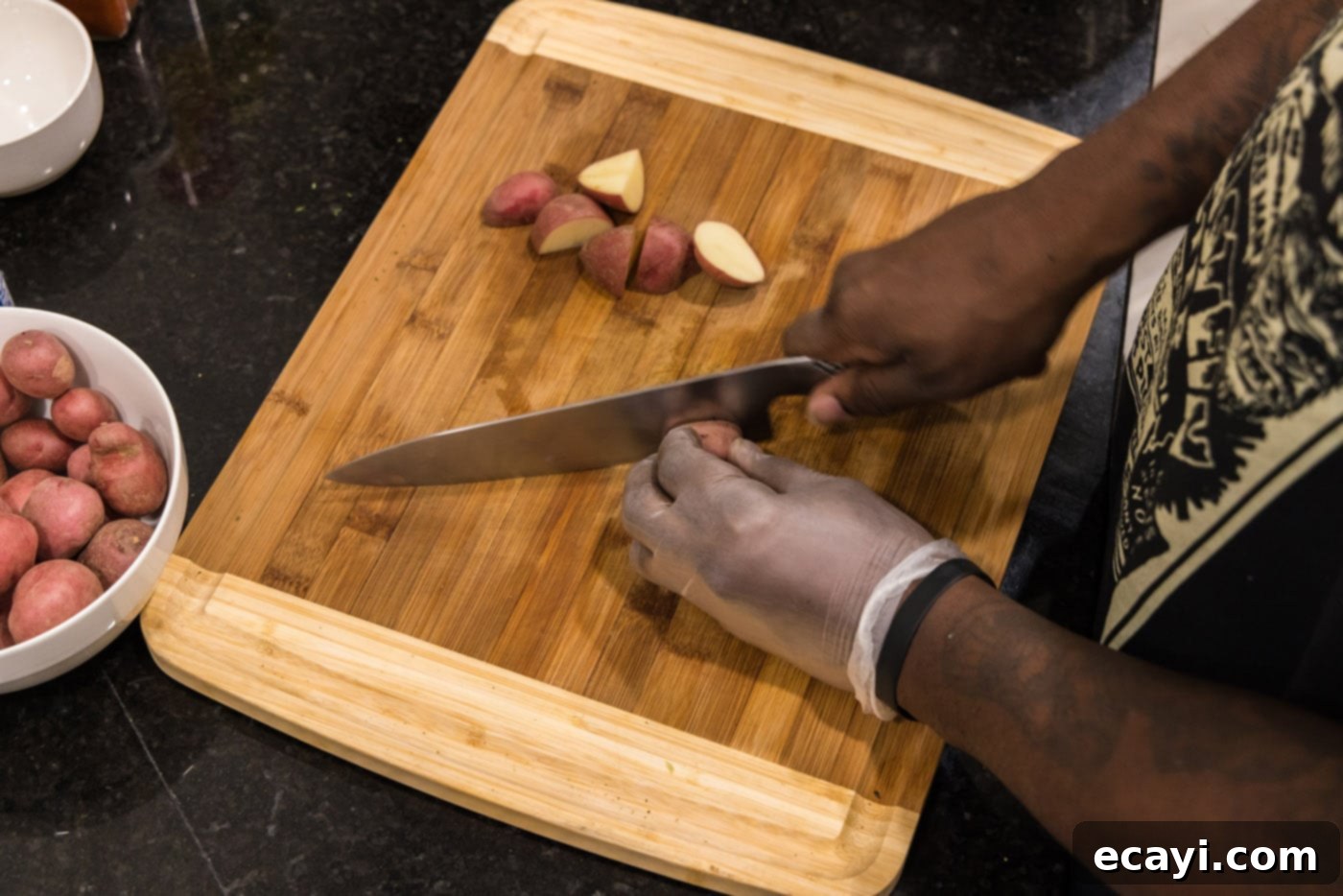 Crispy Roasted Red Potato Medley 5 hands slicing baby red potatoes on a cutting board into even pieces