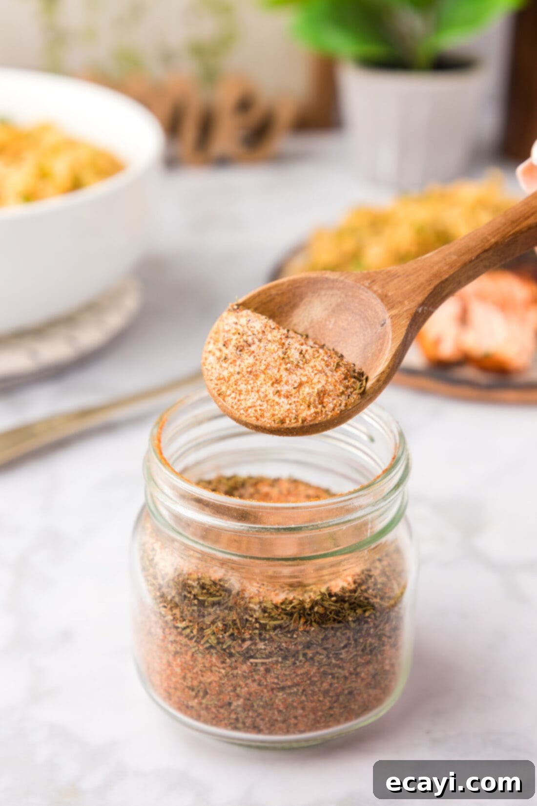 Spicy Louisiana Blend 2 A spoonful of homemade Cajun seasoning being lifted from a glass jar, showcasing its rich, reddish-brown color and coarse texture.