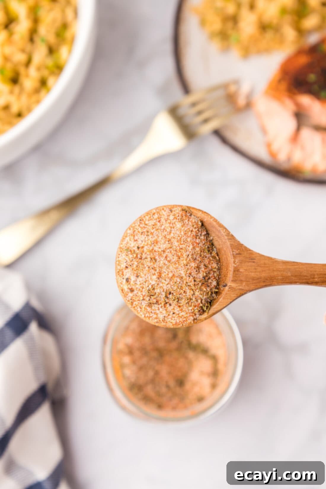 Spicy Louisiana Blend 7 Overhead view of a wooden spoon scooping homemade Cajun seasoning from a jar, highlighting the blend's texture.