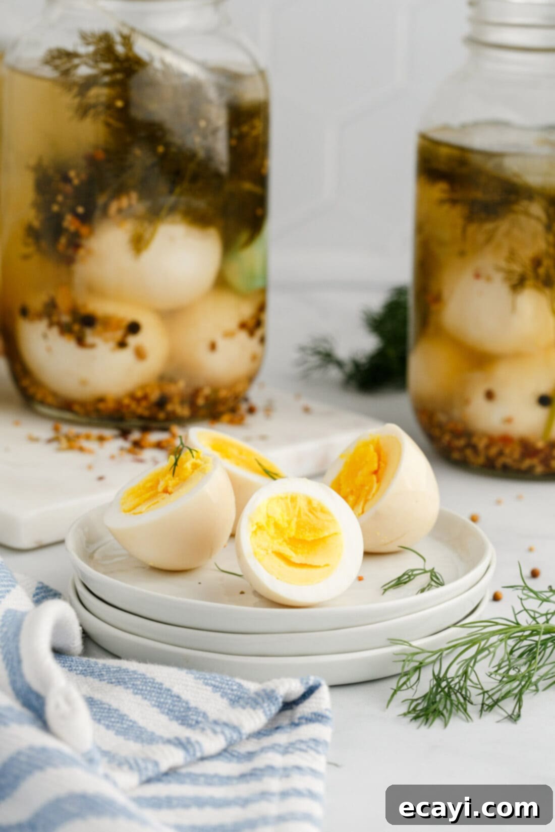 Perfectly Pickled Eggs 11 Two Pickled Eggs cut in half on a plate with jars of Pickled Eggs in the background, showing their golden yolks.