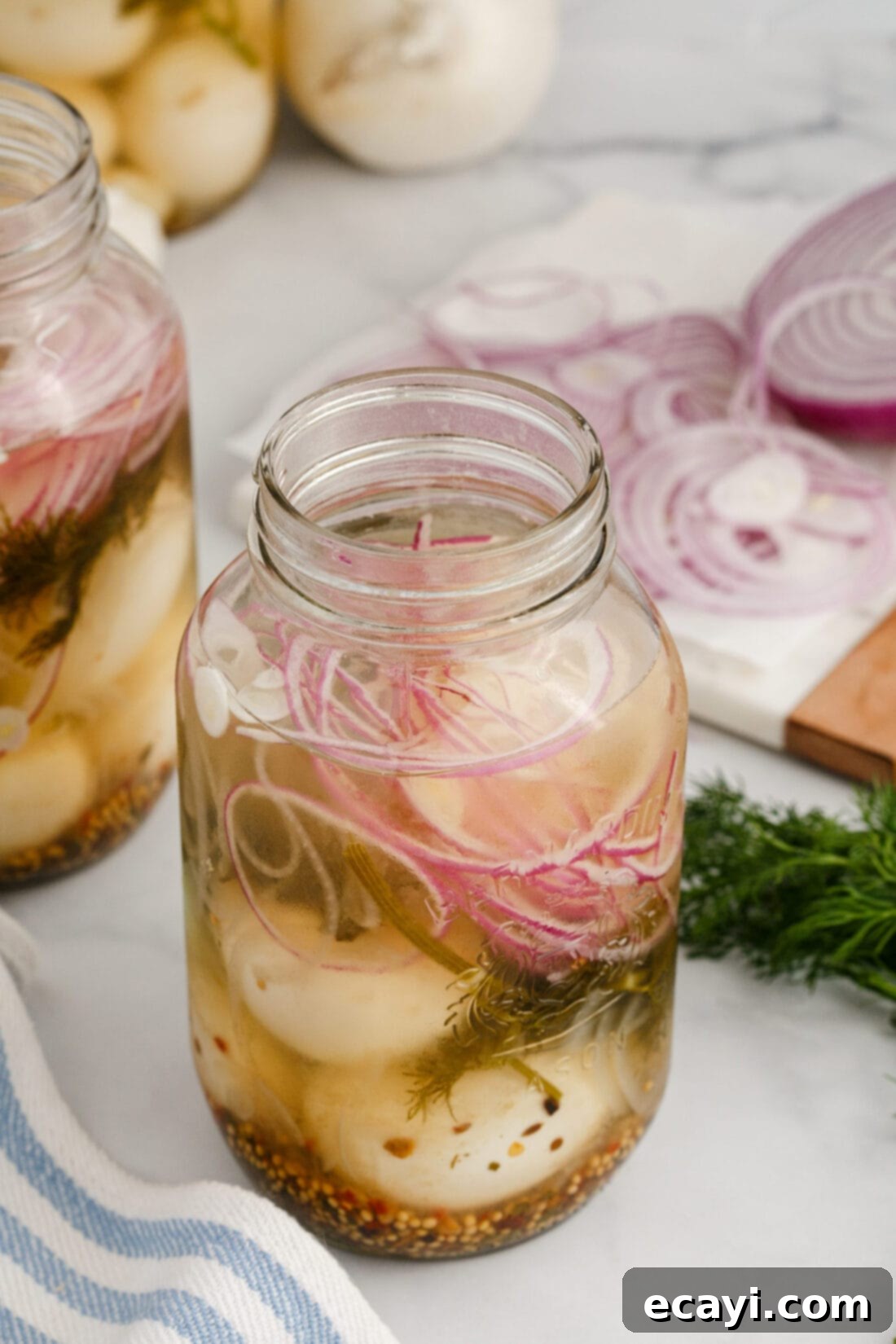 Perfectly Pickled Eggs 3 A clear glass jar filled with golden pickled eggs, vibrant green dill sprigs, and translucent onion slices, ready for refrigeration.