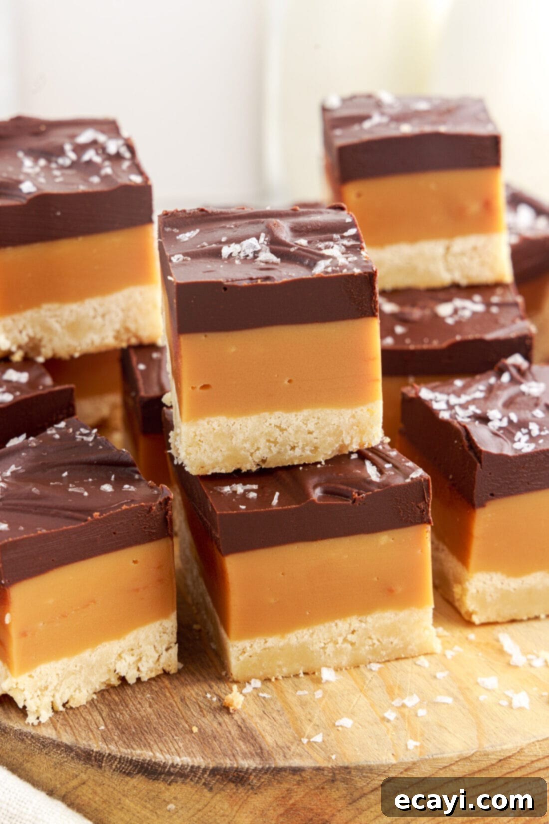 Golden Caramel Indulgence 3 Stacks of freshly cut Millionaire’s Bars beautifully arranged on a rustic wooden board, showing off their distinct layers.