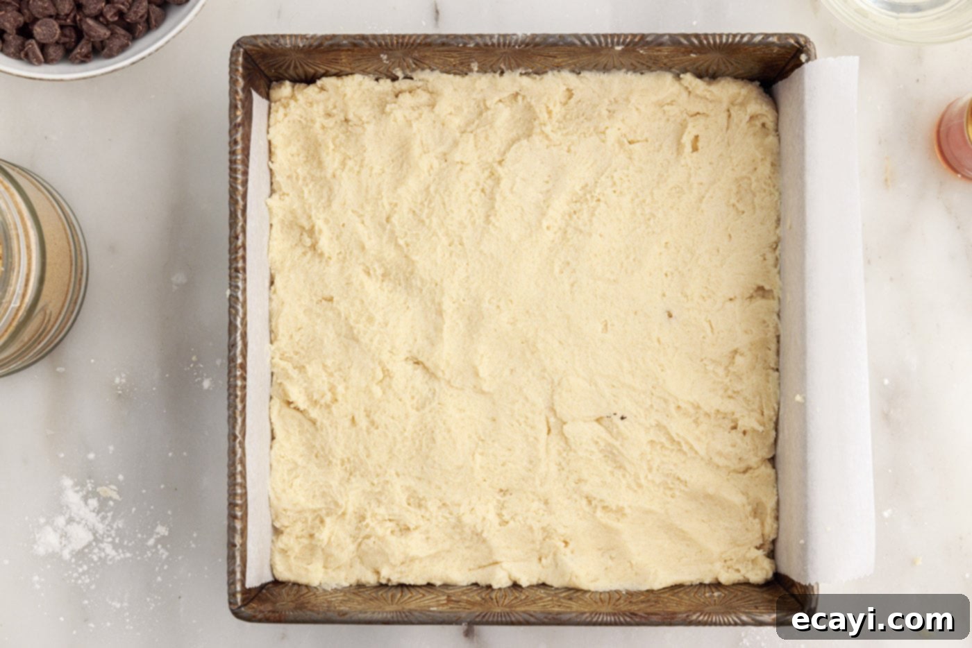 Golden Caramel Indulgence 9 Shortbread crust being pressed evenly onto the bottom of a baking pan lined with parchment paper.
