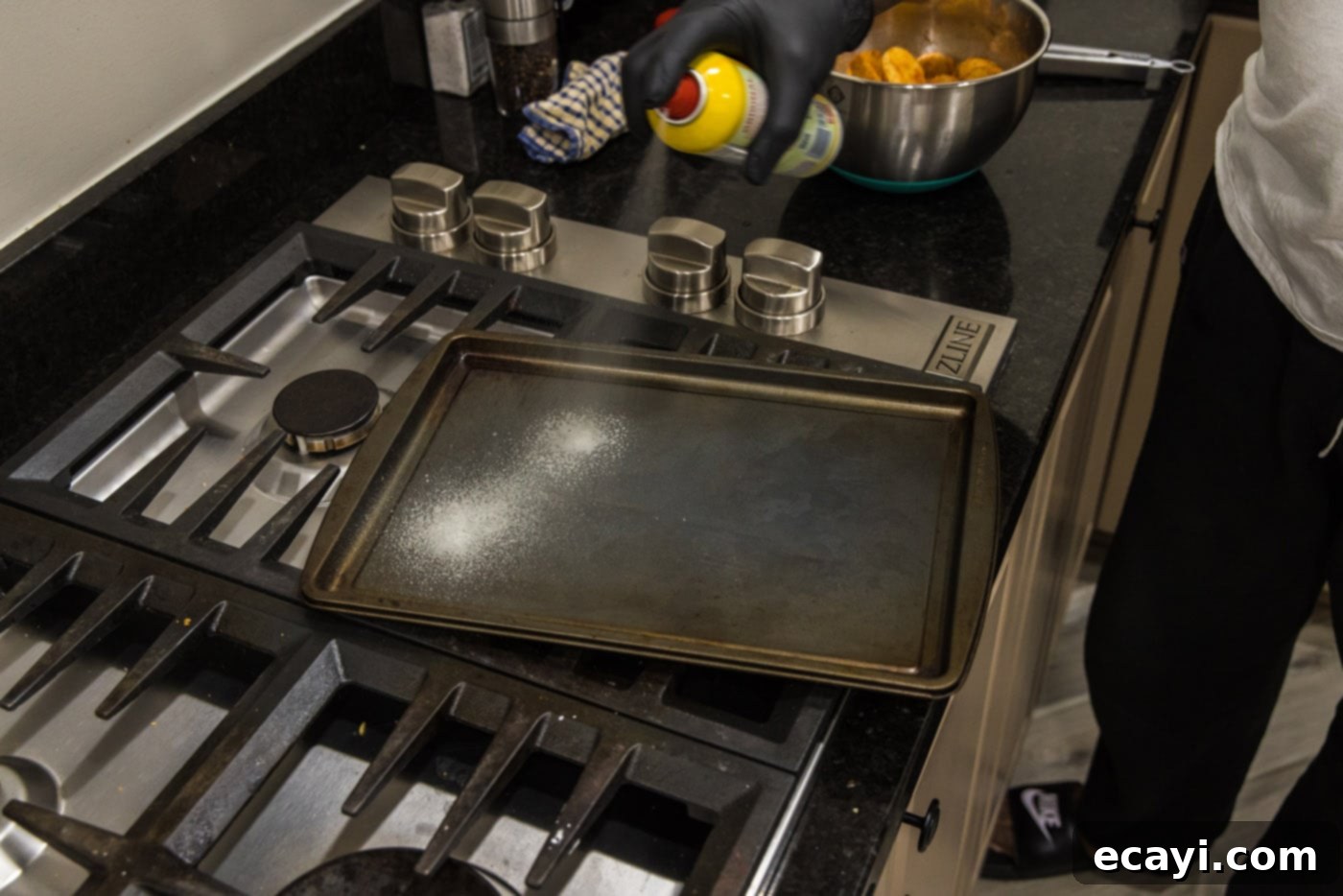 Crispy Parmesan Potatoes 5 A hand spraying a baking sheet with cooking spray, preparing it for potatoes