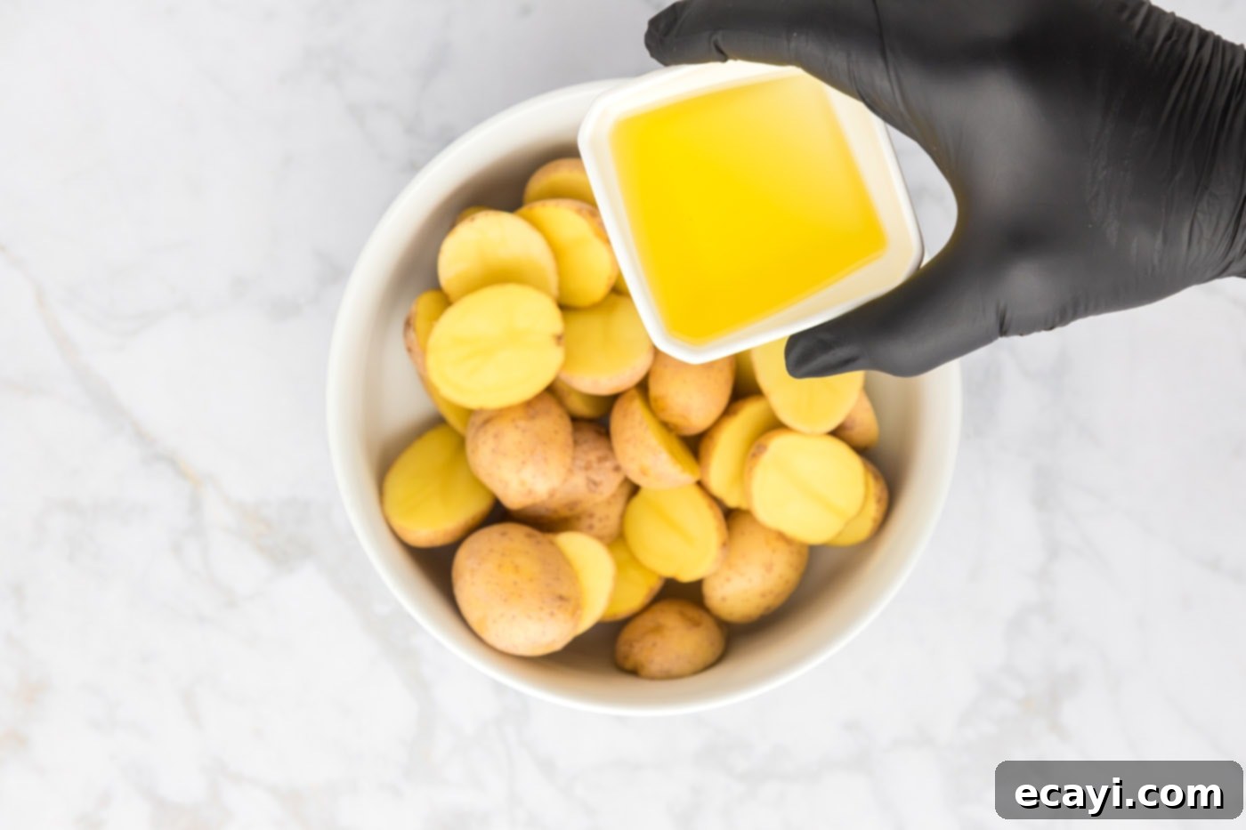 Crispy Parmesan Potatoes 8 Olive oil being poured over sliced potatoes in a bowl