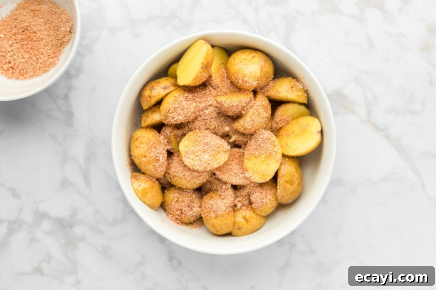 Crispy Parmesan Potatoes 10 Parmesan seasoning mixture sprinkled generously over olive oil-coated sliced potatoes in a bowl