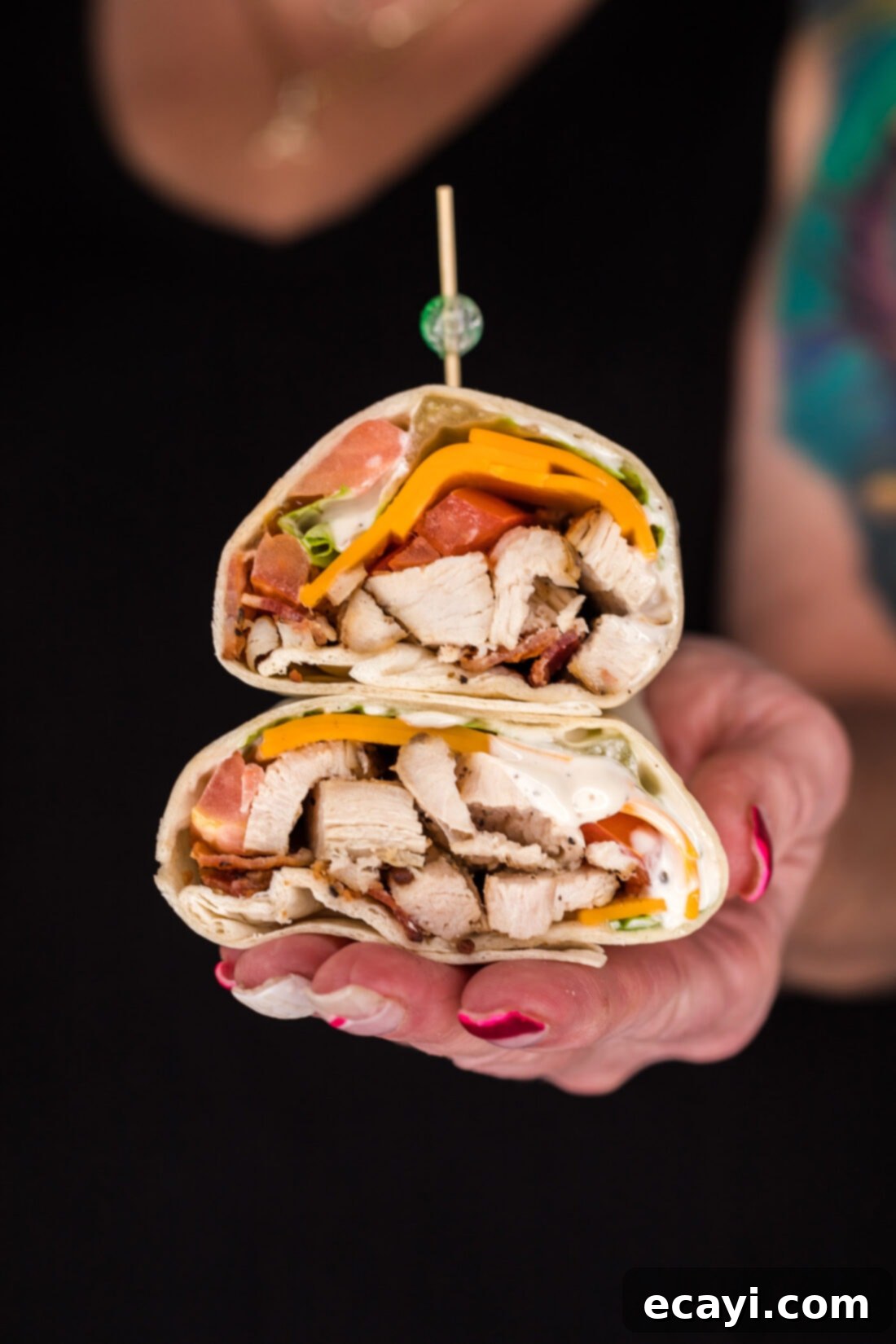 Signature Chicken Bacon Ranch Wrap 3 Hand holding two halves of a Chicken Bacon Ranch Wrap stacked on top of each other, highlighting the rich fillings and perfect roll.