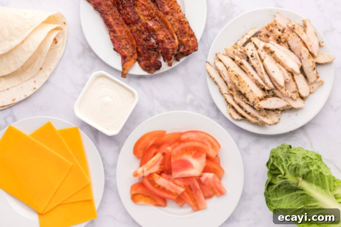 Signature Chicken Bacon Ranch Wrap 4 A flat lay photograph showing all the fresh ingredients for Chicken Bacon Ranch Wrap laid out on a cutting board, including tortillas, chicken, bacon, lettuce, tomatoes, and cheese slices.