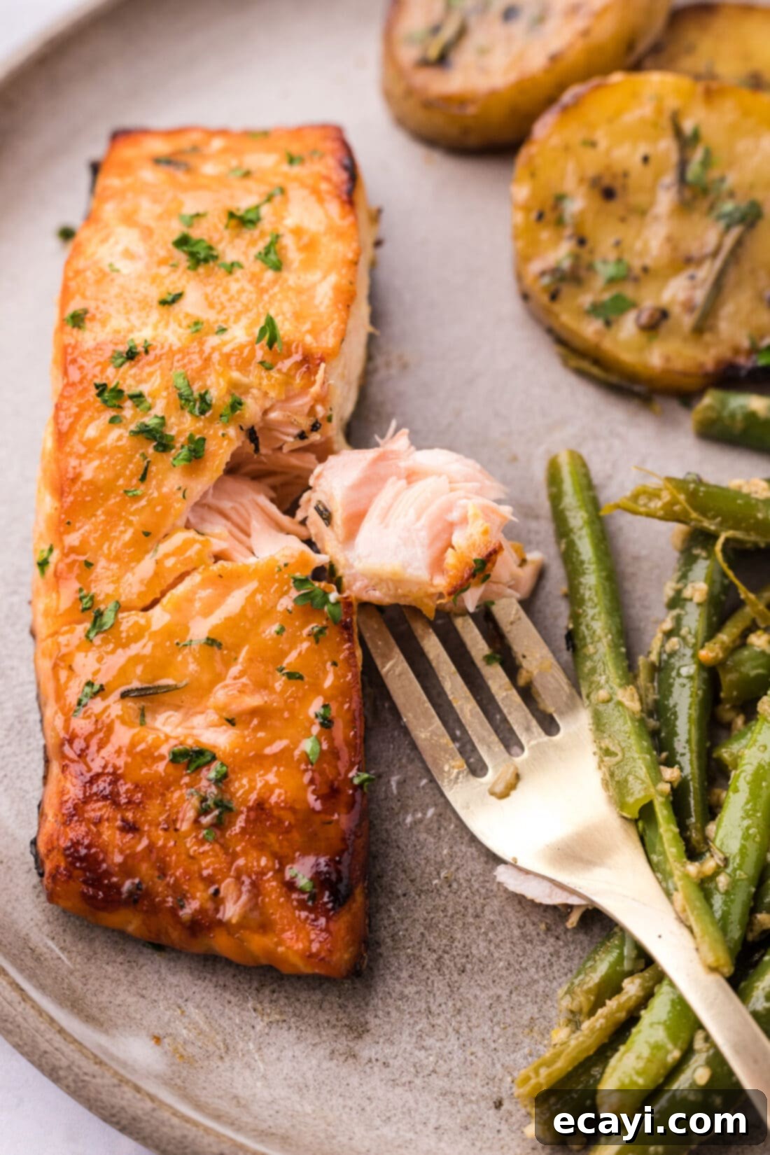 Caramelized Salmon 2 A perfectly cooked piece of Brown Sugar Salmon on a fork, positioned next to a larger salmon fillet on a platter.