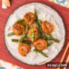 Fiery Hunan Shrimp 11 A vibrant plate of Hunan Shrimp, generously coated in its spicy sauce, served over a bed of white rice with a side of garlic green beans