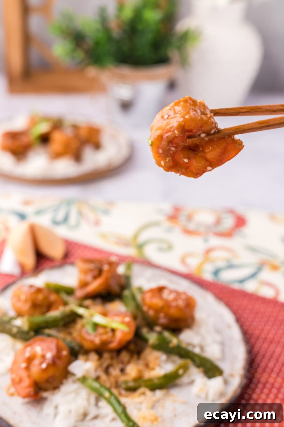 Fiery Hunan Shrimp 3 A pair of chopsticks holding a succulent piece of Hunan Shrimp, showcasing its vibrant sauce and perfect texture.