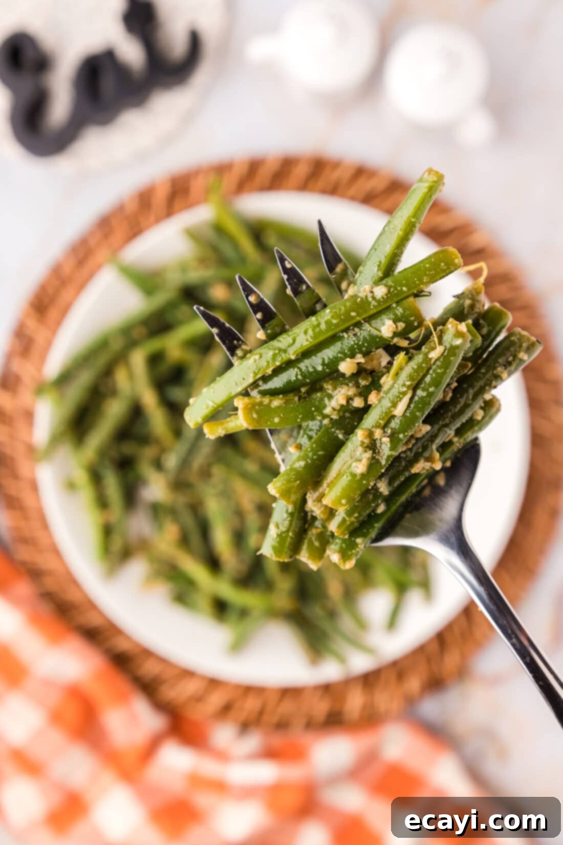 Garlic-Kissed Green Beans 2 Garlic Green Beans on a fork held above a plate of Garlic Green Beans, showcasing their vibrant color and tender texture