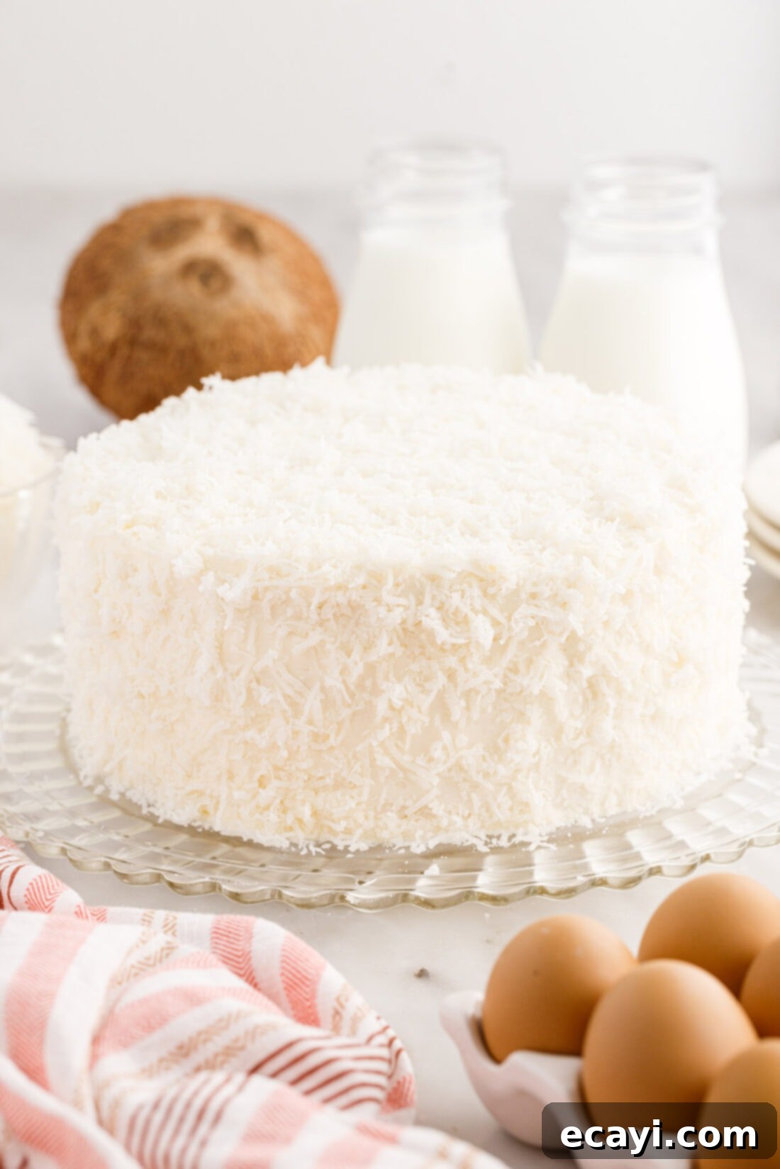 Tropical Cloud Cake 3 Full homemade coconut cake decorated with cream cheese frosting and shredded coconut on a white cake stand